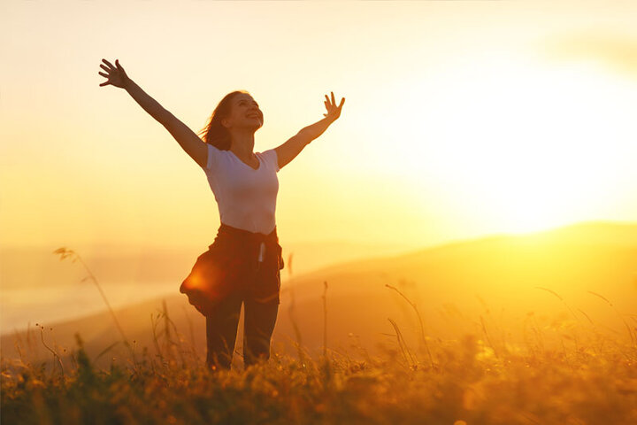 girl in field arms stretched up taking in the suns rays